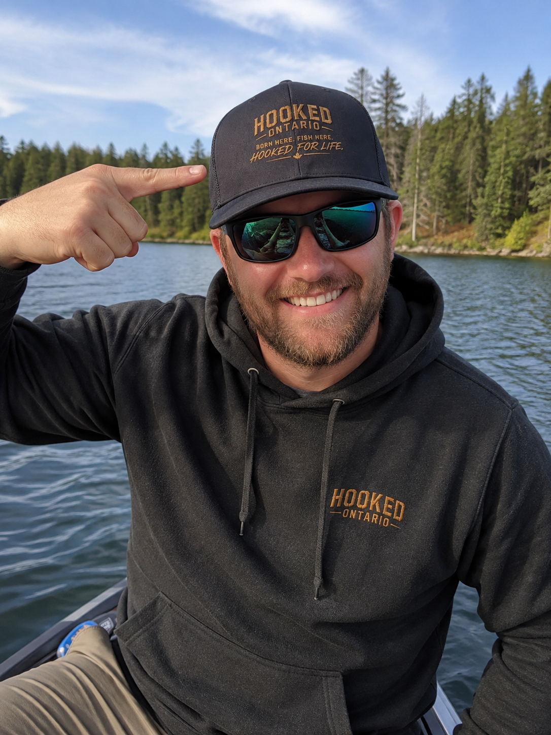 Angler on a lake pointing at his black Hooked Ontario trucker cap and hoodie